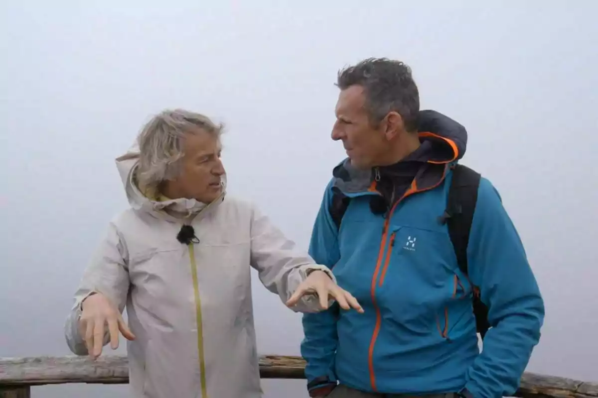 Dos personas conversando al aire libre en un día nublado, ambas con chaquetas y mochilas. Dos personas conversando al aire libre en un día nublado, ambas con chaquetas y mochilas.