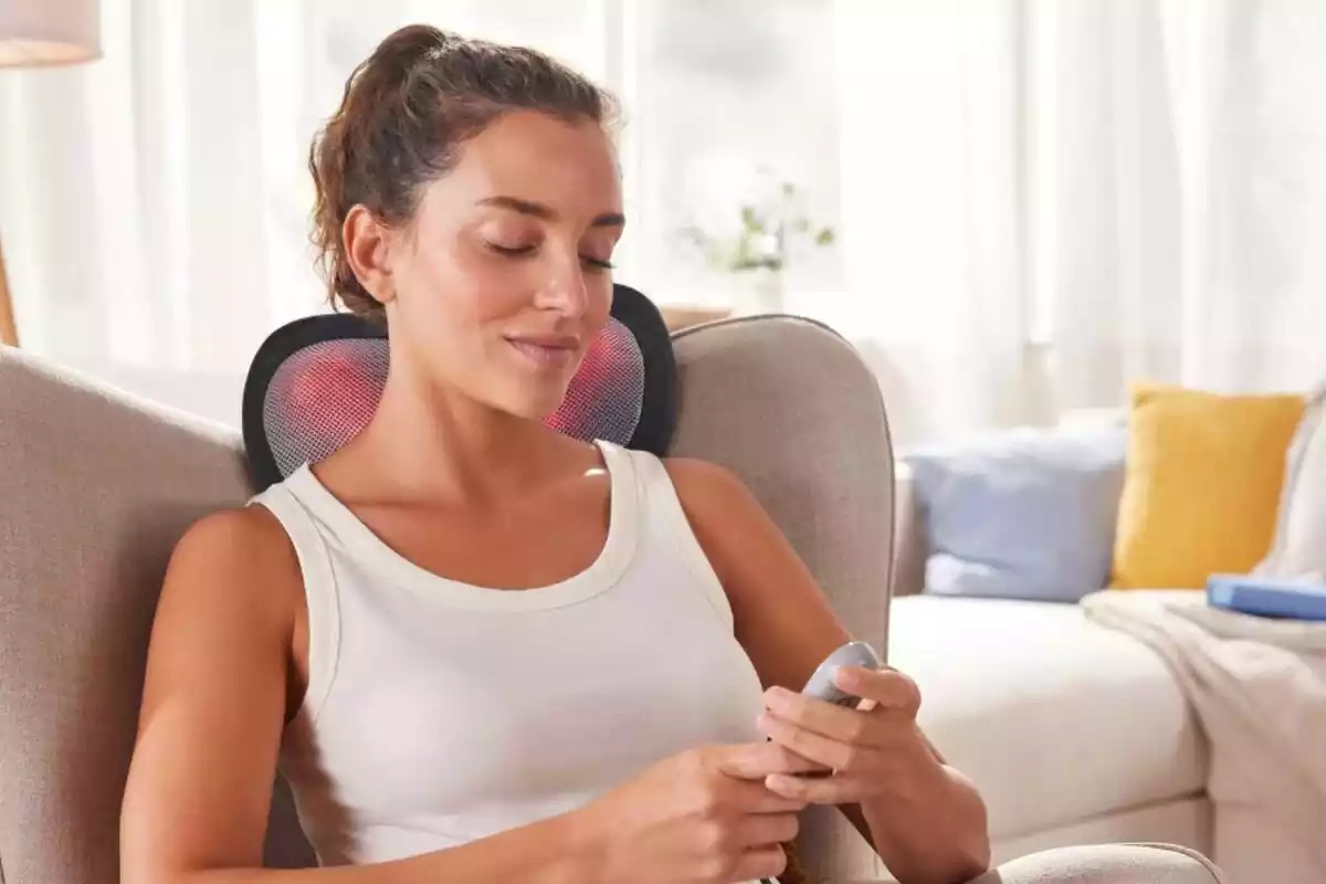 Mujer relajándose en un sillón con un masajeador de cuello y un control remoto en las manos.