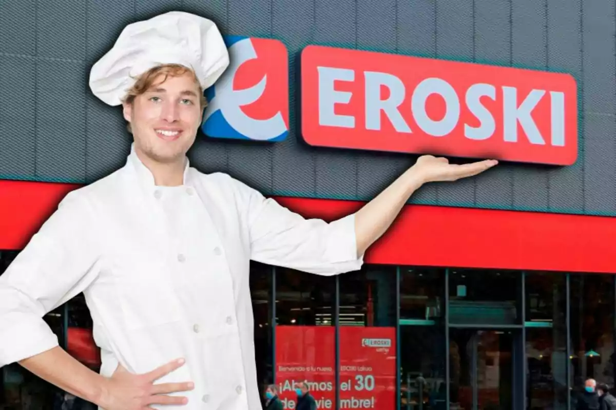 Un chef sonriente con uniforme blanco y gorro de cocinero está frente a una tienda Eroski, señalando el letrero con una mano.