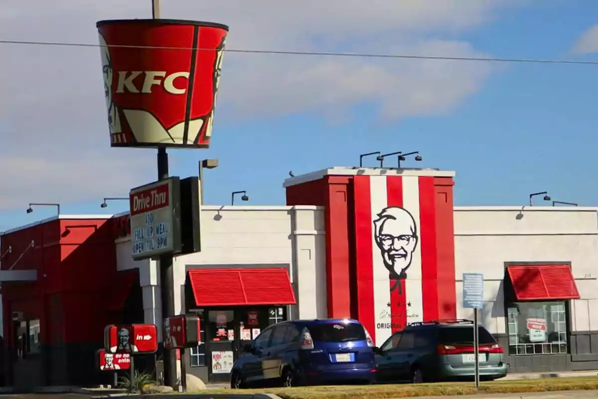 Un restaurant de menjar ràpid amb un gran cubell de pollastre fregit com a rètol -que és KFC- i un mural del fundador a la façana. Un restaurant de menjar ràpid amb un gran cubell de pollastre fregit com a rètol -que és KFC- i un mural del fundador a la façana.