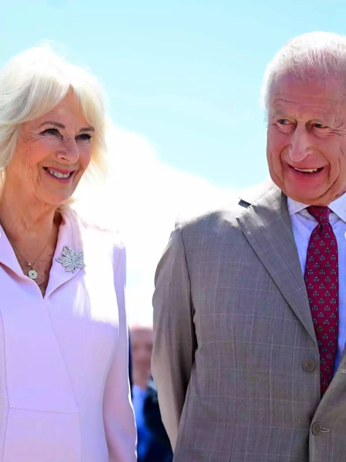El rei Carles III i la reina consort Camila somriuen mentre està dreta a l’aire lliure sota un cel blau.