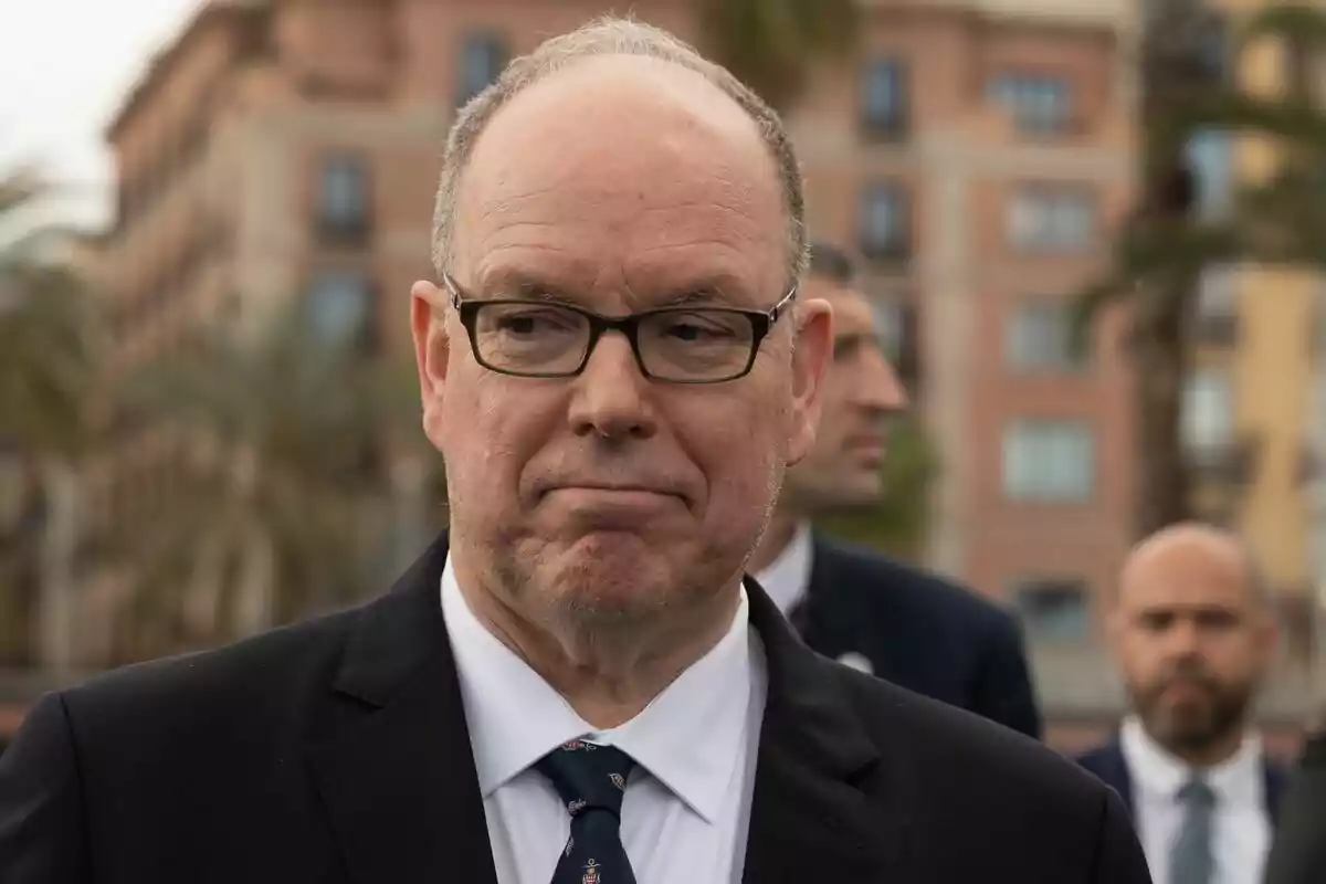 A man with glasses and a dark suit in an urban setting.