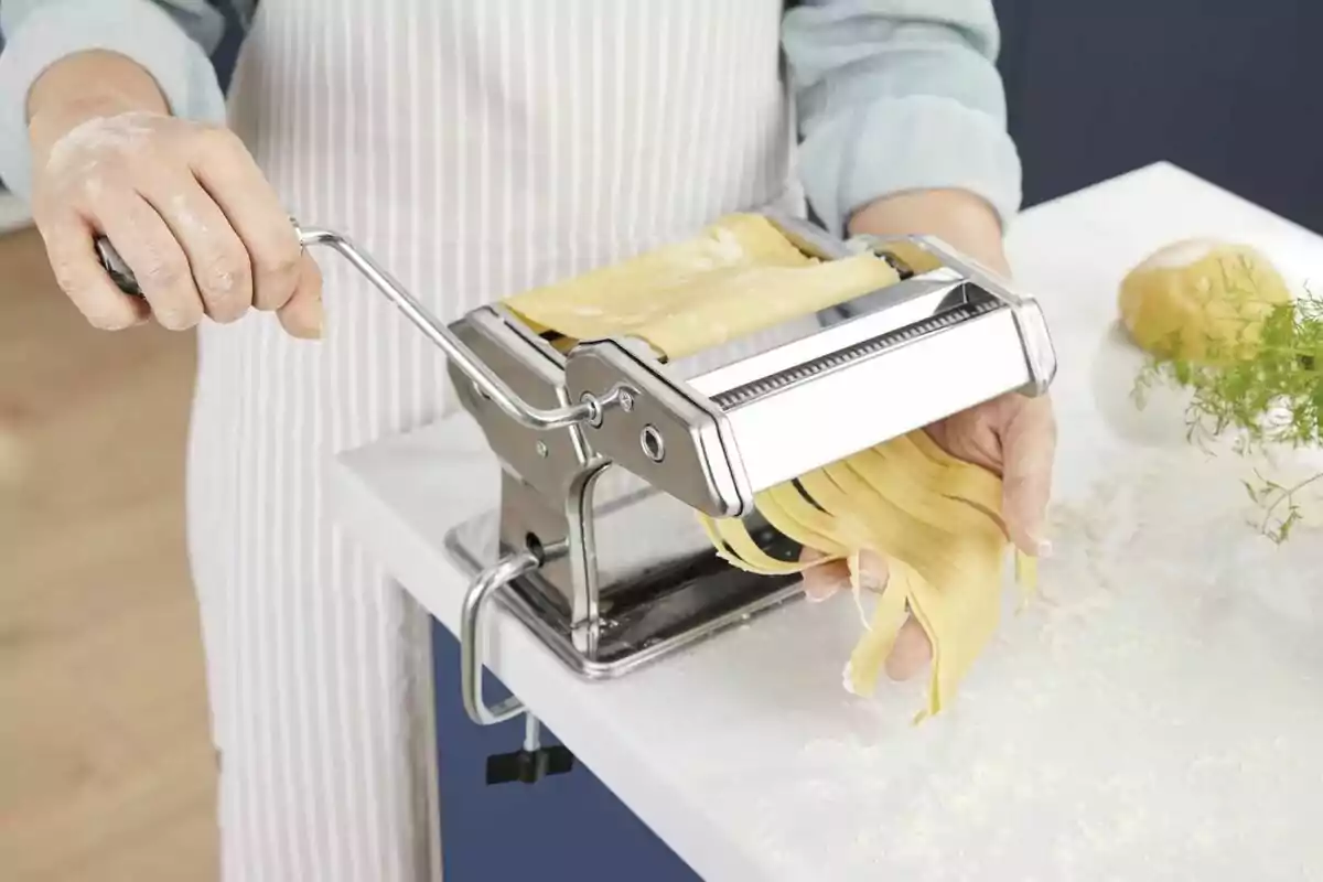 Persona usando una máquina para hacer pasta fresca en una cocina.