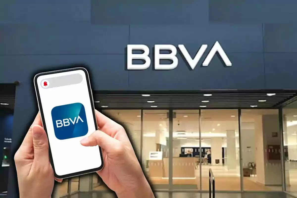 Una persona sostiene un teléfono móvil con el logo de BBVA frente a una sucursal del banco.