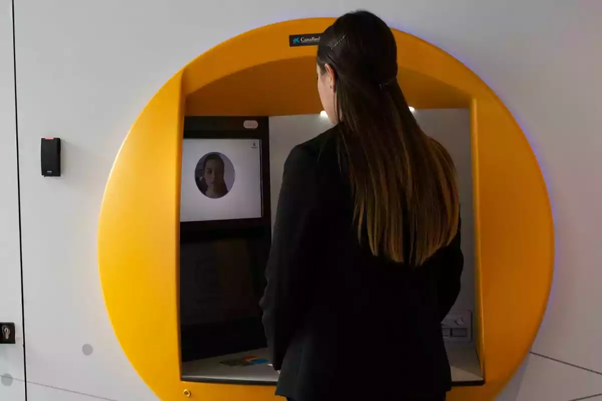 Una mujer utilizando un cajero automático de Caixabank con un diseño moderno y una pantalla que muestra su rostro.