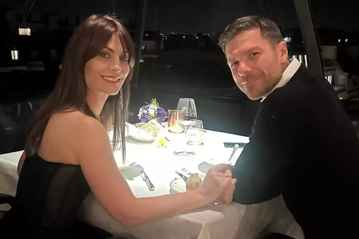 Nagore Aranburu i Xabi Alonso asseguts a una taula de restaurant elegantment decorada, agafats de les mans i somrient a la càmera.