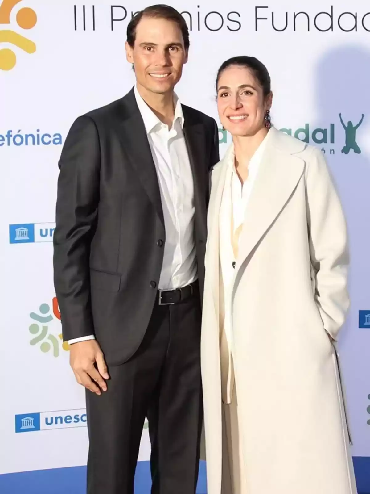 Rafa Nadal and Xisca Perelló pose together at a formal event with a background displaying organization logos.