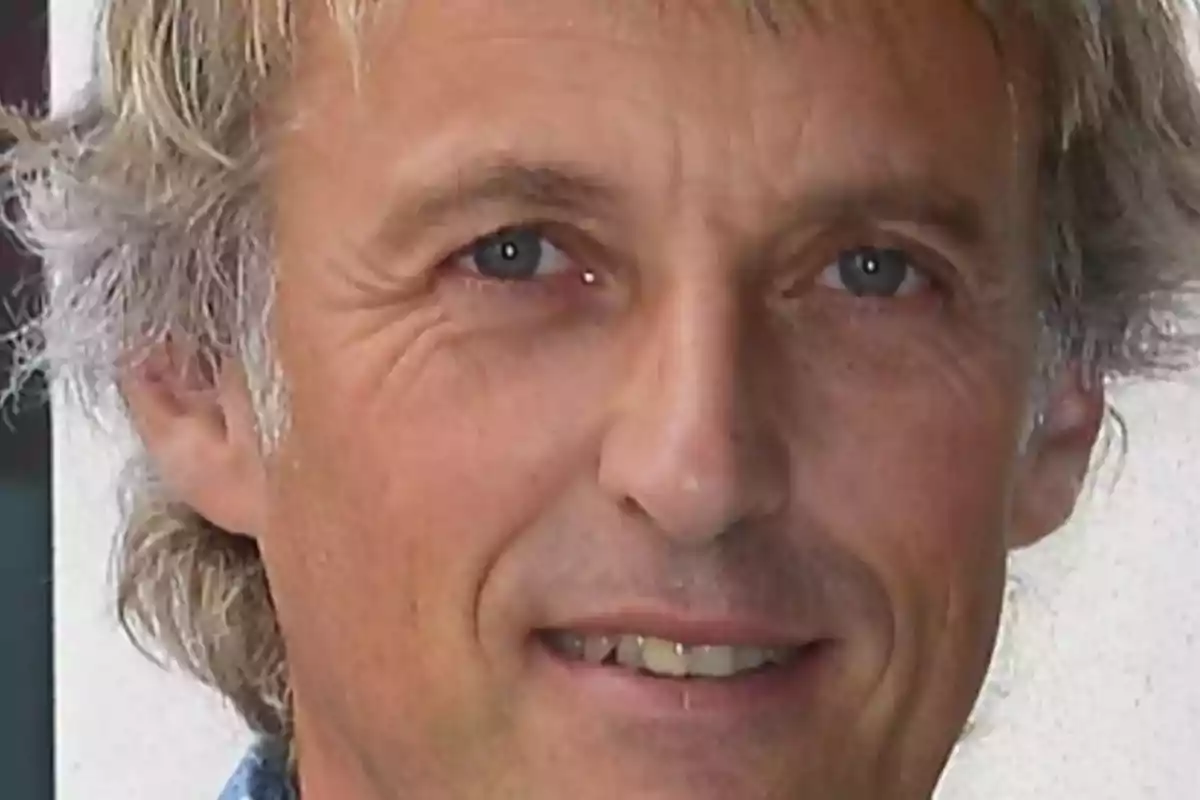 Un hombre de cabello canoso y ojos azules sonríe ligeramente mirando hacia la cámara.