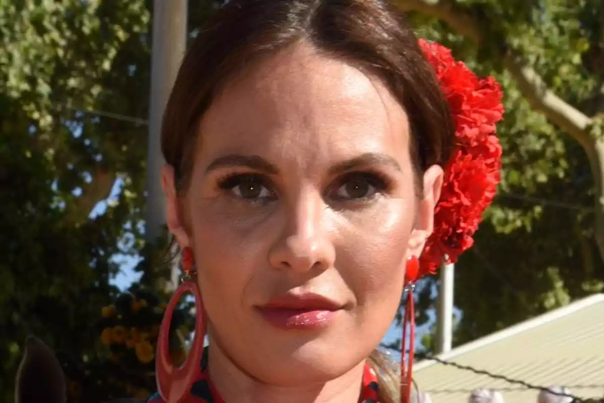 Primer plano de Jessica Bueno seria con una flor roja en el pelo y unos grandes pendientes en la Feria de Abril de Sevilla