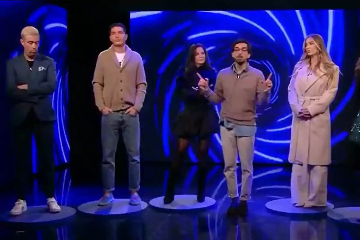 Javier Mouzo, Álex Ghita, Ana Herminia, Dani Santos y Romina Malaspina de personas está de pie en un escenario con un fondo azul brillante en GH DÚO.