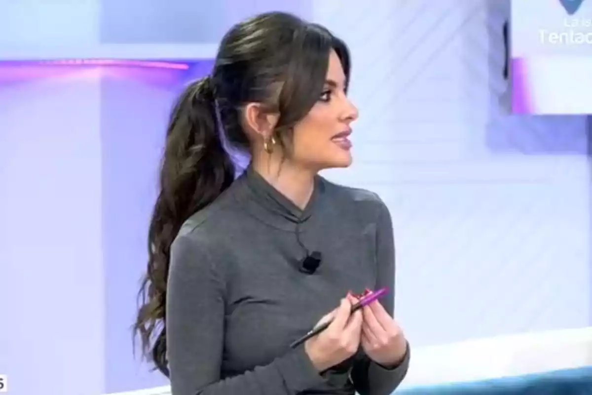 Alexia Rivas con cabello largo y oscuro recogido en una coleta, vestida con un suéter gris, sostiene un bolígrafo rosa mientras parece estar hablando en un entorno de estudio de televisión. Captura de 'Vamos a ver'