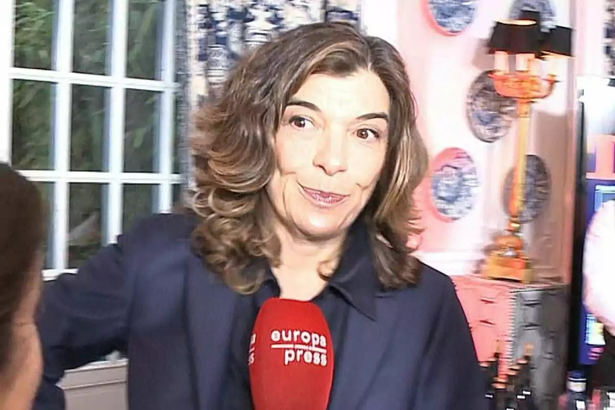 Xandra Falcó con los labios apretados en traje negro y un micrófono rojo delante Xandra Falcó con los labios apretados en traje negro y un micrófono rojo delante